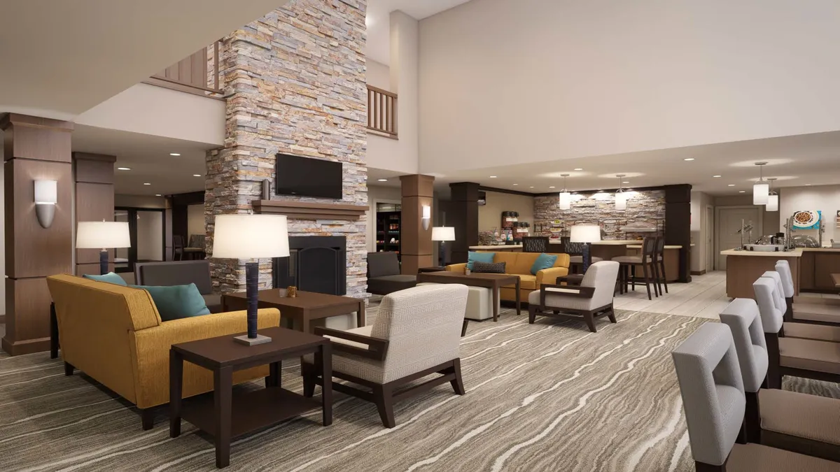 This image showcases a cozy living area with a stone fireplace, comfortable sofas, and a relaxed, welcoming ambiance. The layout encourages socializing, with ample seating arranged for conversation or unwinding, and warm lighting that adds to the inviting atmosphere. The reception area is visible but unobtrusive, suggesting an open-plan design.
