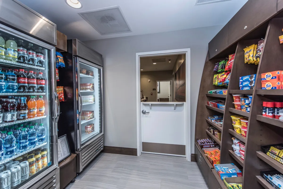 This image presents a convenient in-suite snack and beverage area, featuring a refrigerated drink display and snack shelves by the entrance. The setup is clean and inviting, catering to guests’ convenience and comfort during their stay.