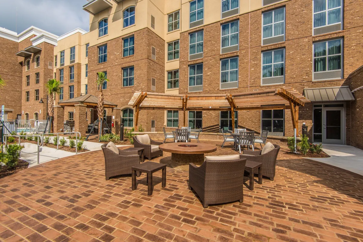An inviting outdoor fire pit area surrounded by comfortable seating and lush landscaped greenery. The scene is bathed in the warm glow of sunset, creating a cozy and communal atmosphere perfect for social gatherings or relaxing evenings under the stars.