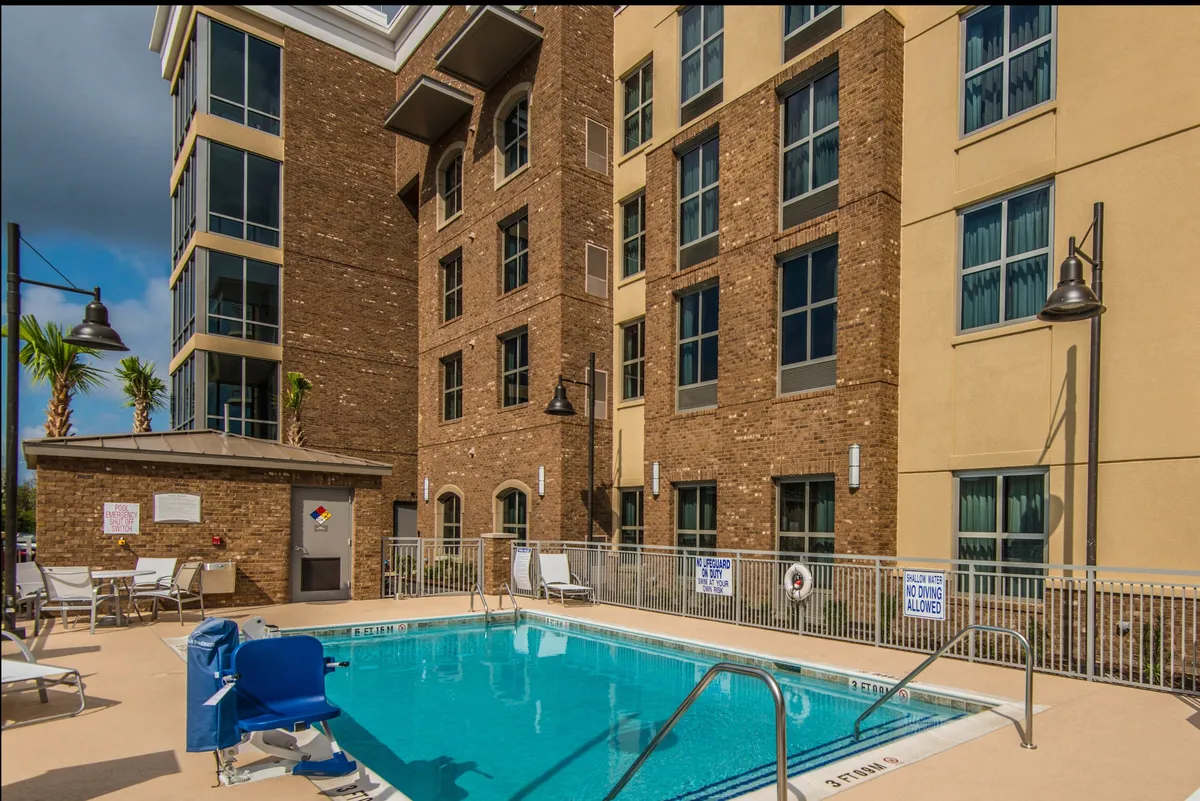 This image showcases the outdoor swimming pool surrounded by lounge chairs, palm trees, and the hotel's exterior buildings. The setting is lively and inviting, with ample space for families to relax or splash in the pool under the sun.