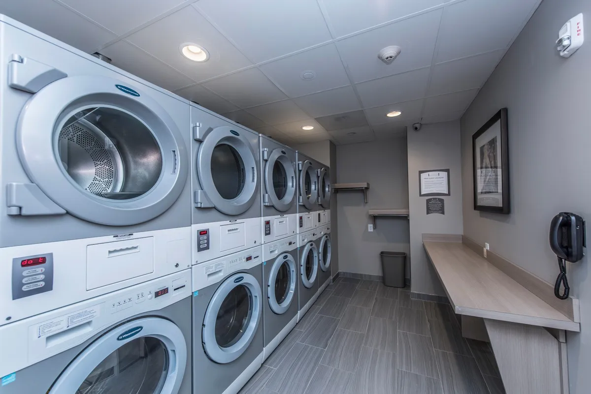 A functional laundry room featuring a row of modern washing machines, a folding counter, and clear signage. The organized, efficient space offers practical amenities for longer stays, making it easy for guests to manage laundry during their visit.
