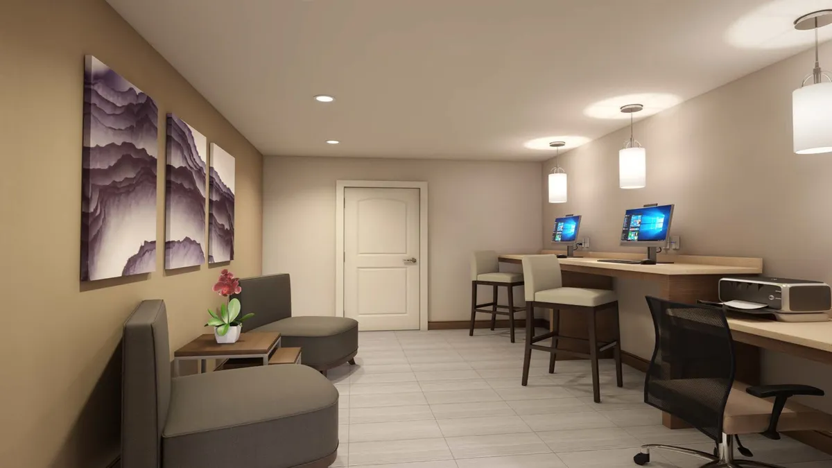 This interior image features a comfortable seating area alongside computer stations and framed artwork, blending a casual lounge space with a workspace. The setting looks conducive to both productivity and relaxation, with soft lighting and contemporary decor.